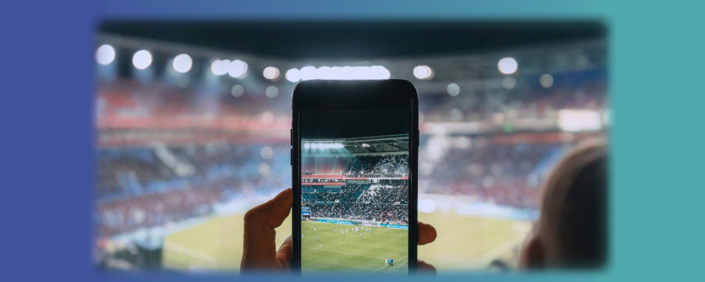 Headergrafik mit Smartphone, mit dem ein Foto im Stadion gemacht wird. Symbolbild für User-generated Content (UGC)